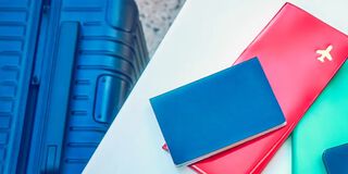 A woman sitting at a table next to her suitcase with a smartphone, passport and plane ticket.