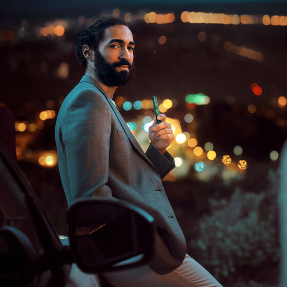 Confident man in a gray suit holding an IQOS device at night with blurred city lights in the background.