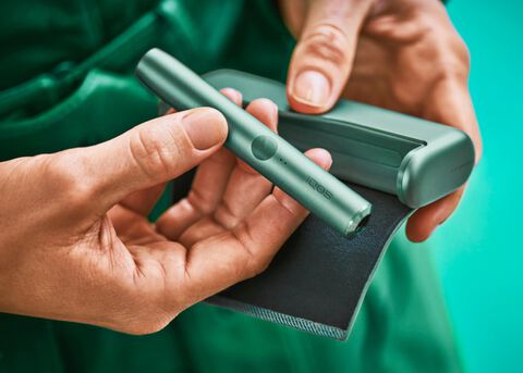 Close up of hands holding IQOS ILUMA jade green device.
