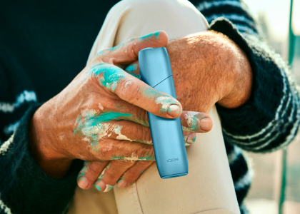 Hands holding a turquoise IQOS Originals One heated tobacco device.