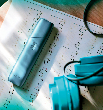 IQOS Originals One device on a music sheet, next to turquoise headphones.