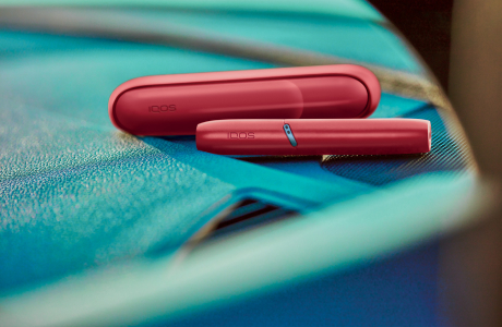 Hands holding a turquoise IQOS Originals One heated tobacco device.